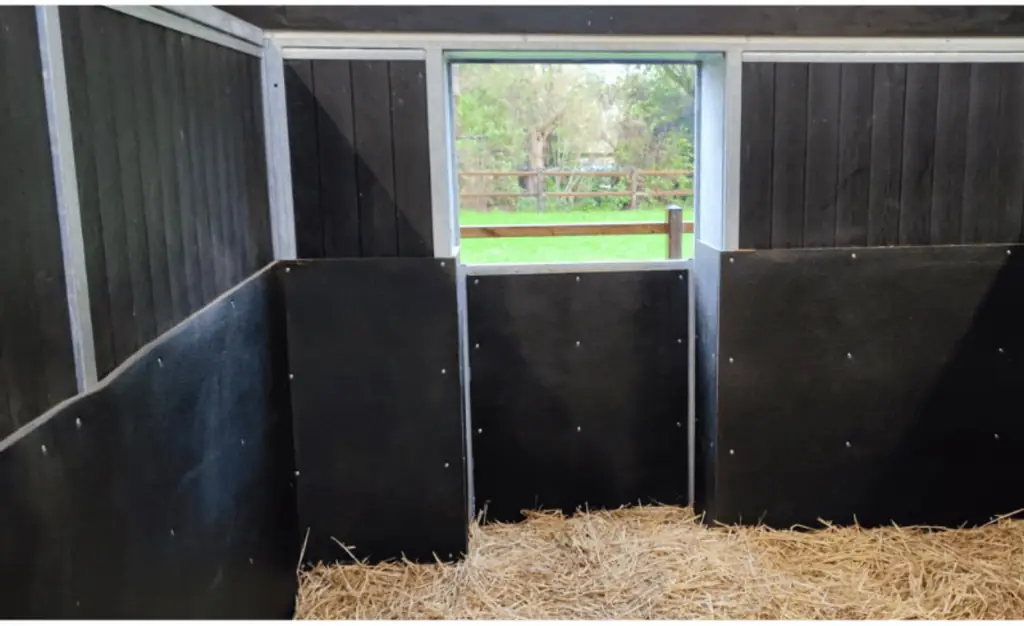 Paardenbox met zwarte rubber stalwandbekleding tegen de wanden en stro op de vloer